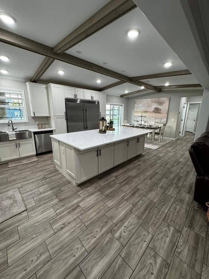 Modern kitchen with a spacious layout featuring a large white island, wood-beam ceiling, and light wood tile flooring. Comforting, airy ambiance.