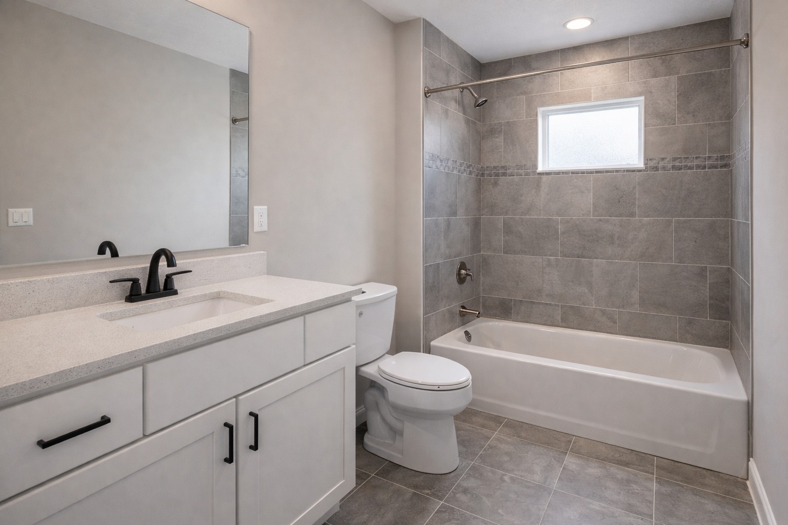 Modern bathroom with a gray tiled shower, white bathtub, white vanity with black fixtures, and a large mirror. A small window provides natural light.