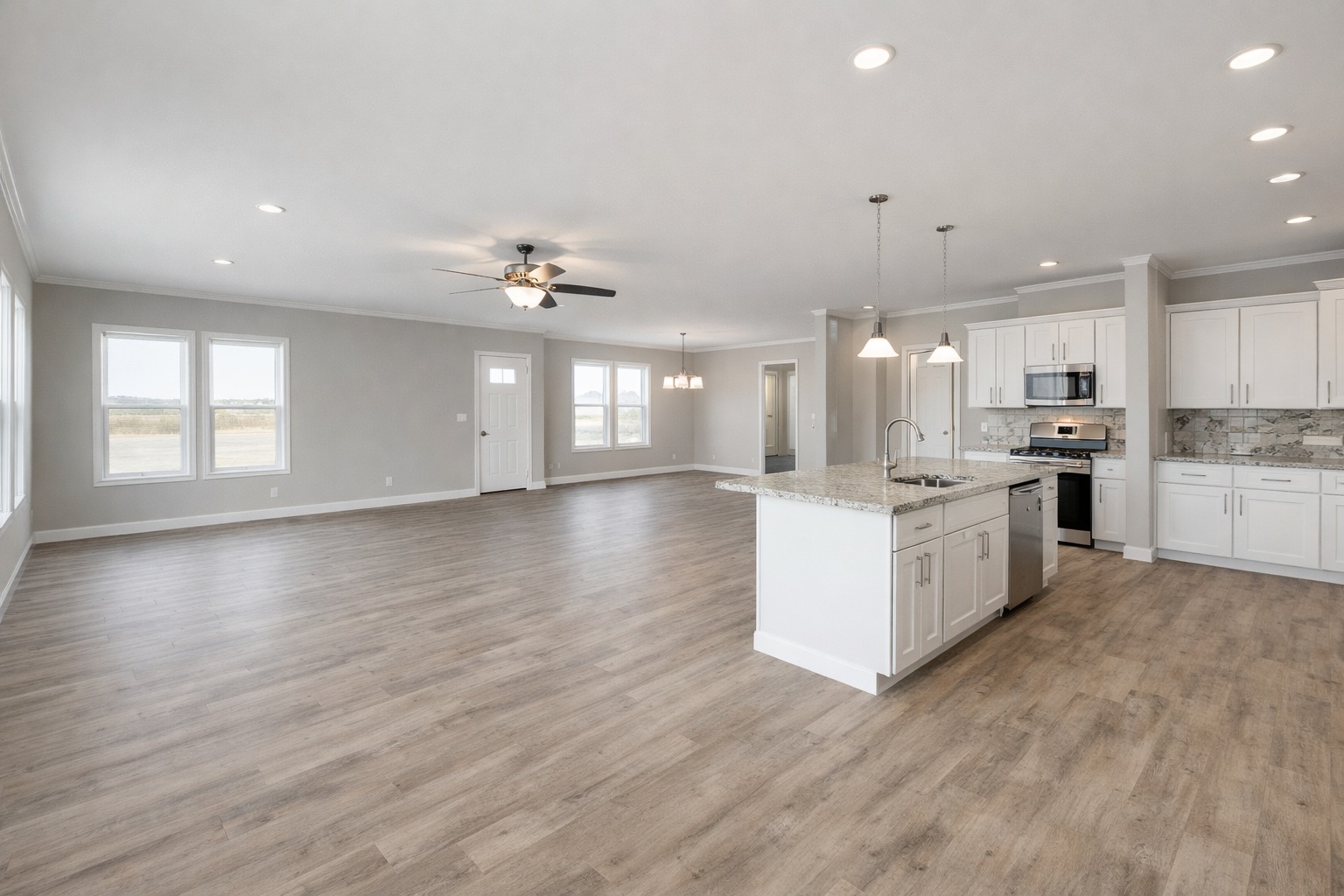 Spacious open-plan kitchen and living area with light wood flooring. Features a modern kitchen with white cabinets, granite island, and stainless steel appliances.