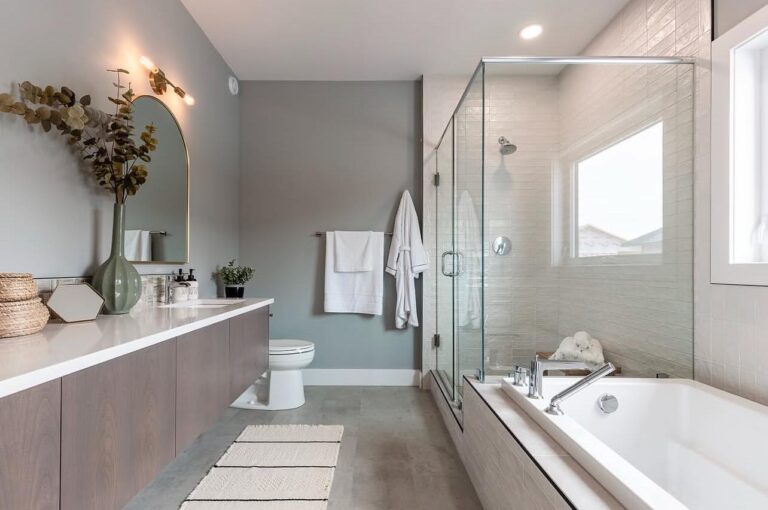 A modern bathroom with a minimalist design features a glass shower, a bathtub, and a large mirror. Neutral tones create a calm and clean atmosphere.