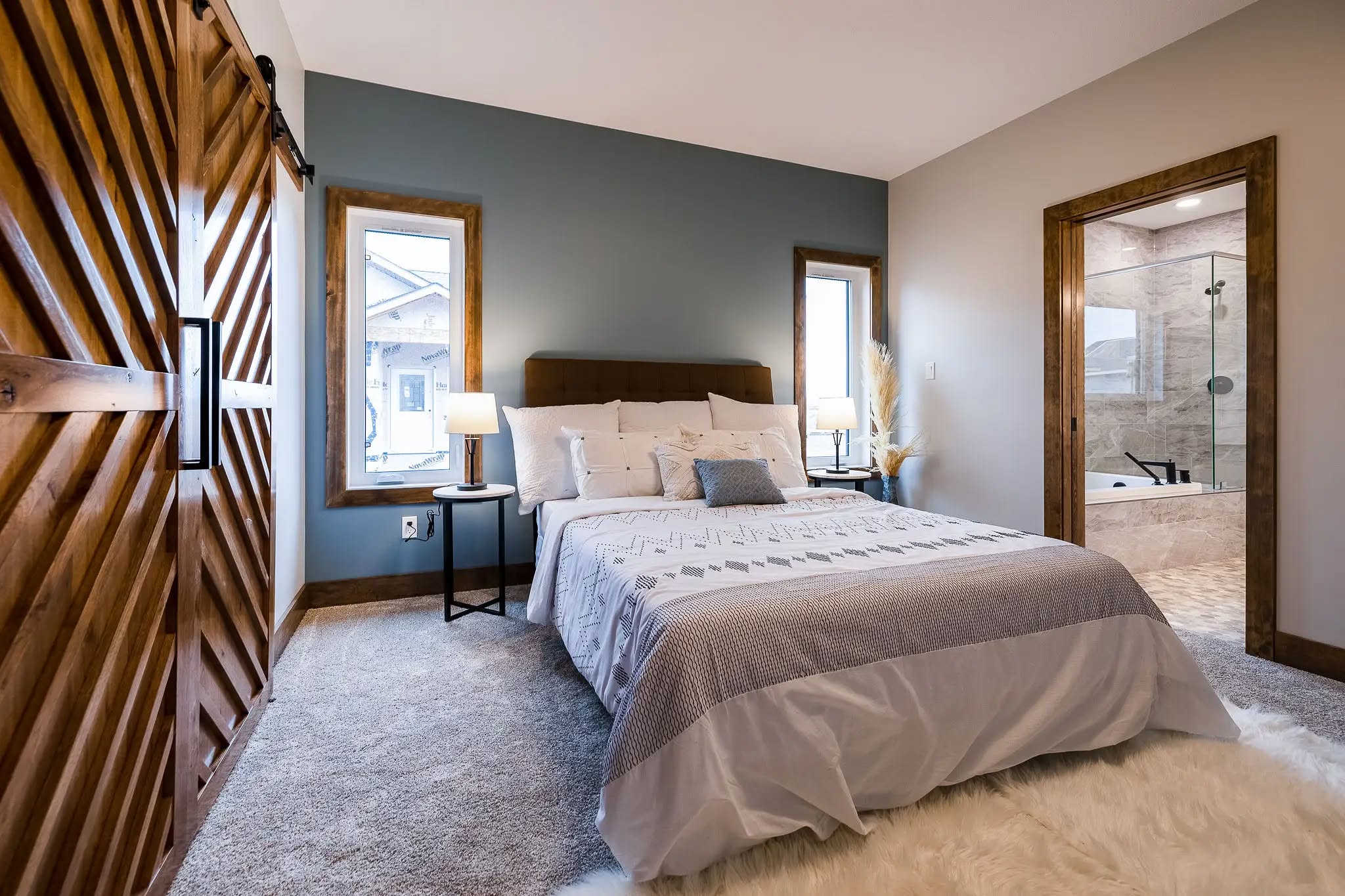 A cozy bedroom with a large bed, blue accent wall, wooden sliding door, and a view of the attached bathroom. Soft lighting creates a calm ambiance.