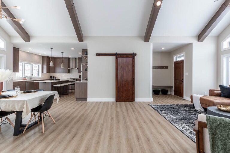 Spacious modern living area with wooden floors, exposed beams, and a sliding barn door. Includes a dining table, open kitchen, and comfortable seating.