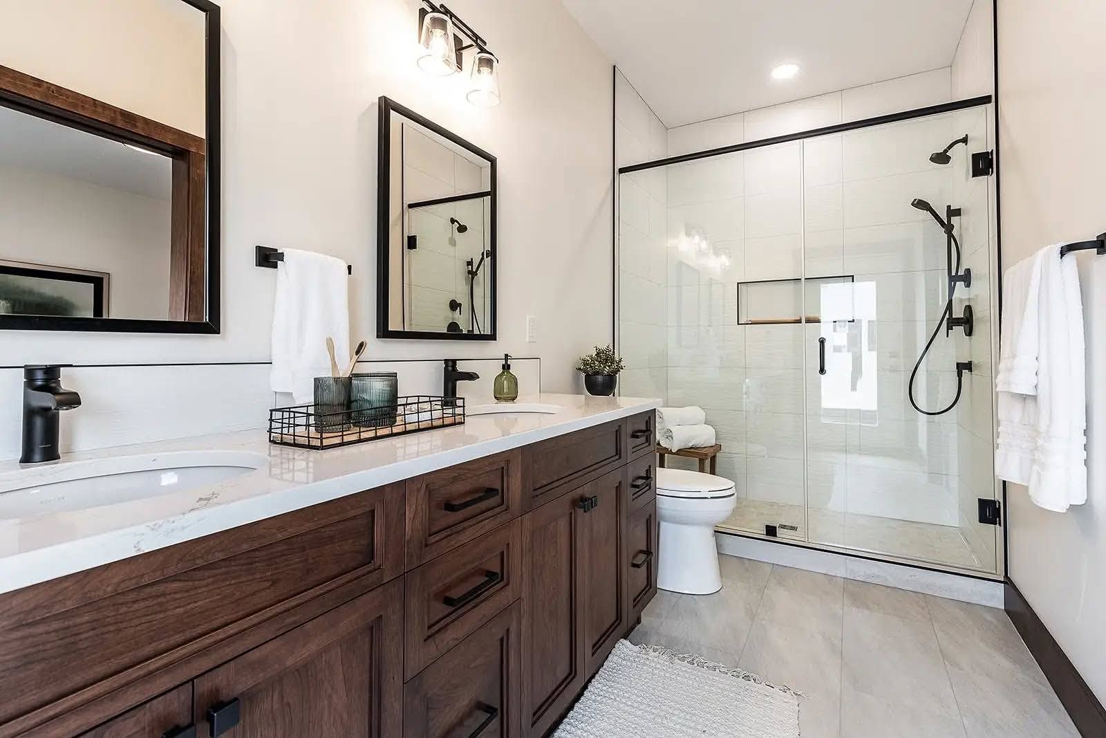 Modern bathroom with a wooden vanity, dual sinks, and large mirrors. Glass shower enclosure with black fixtures, white tiles, and soft lighting.