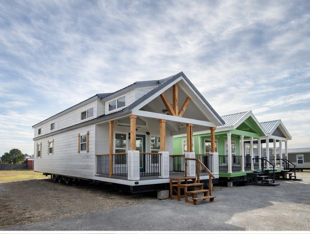 Row of tiny houses with white and green facades, wooden beams, and porches under a partly cloudy sky, conveying a sense of modern simplicity.