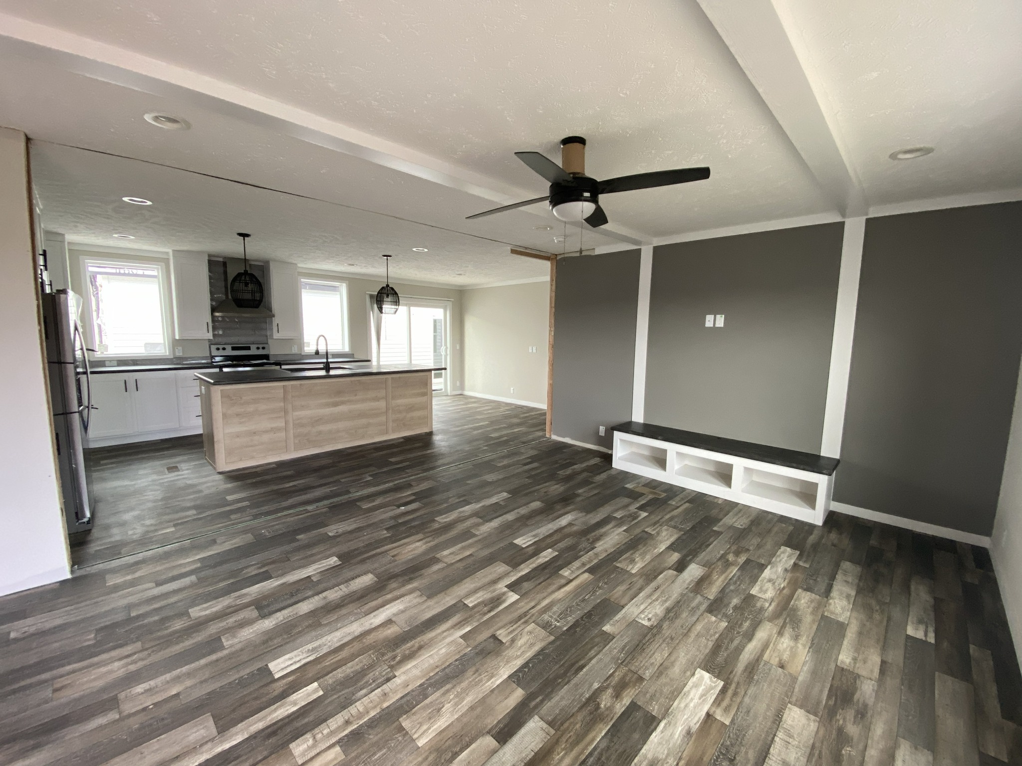Spacious open-concept kitchen and living room with dark wood flooring, gray walls, black ceiling fan, and wooden island. Modern and minimalist design.