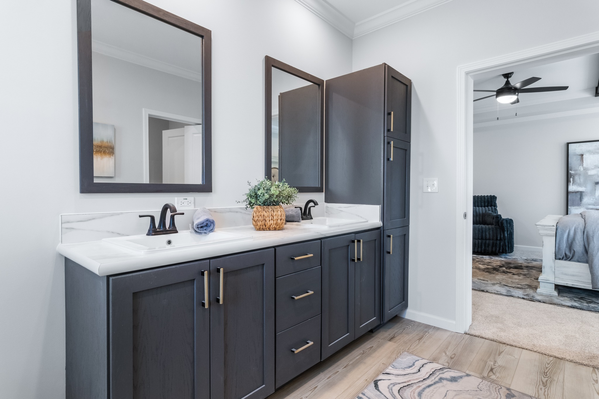 Elegant bathroom with dark wood cabinets and dual sinks, featuring two rectangular mirrors. A bedroom is visible through the doorway, conveying a modern, serene atmosphere.