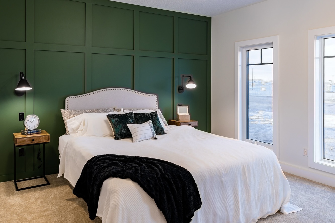 Elegant bedroom with a green accent wall features a white bed, velvet pillows, plush black throw, bedside tables, and modern lamps. Soft, calming ambiance.