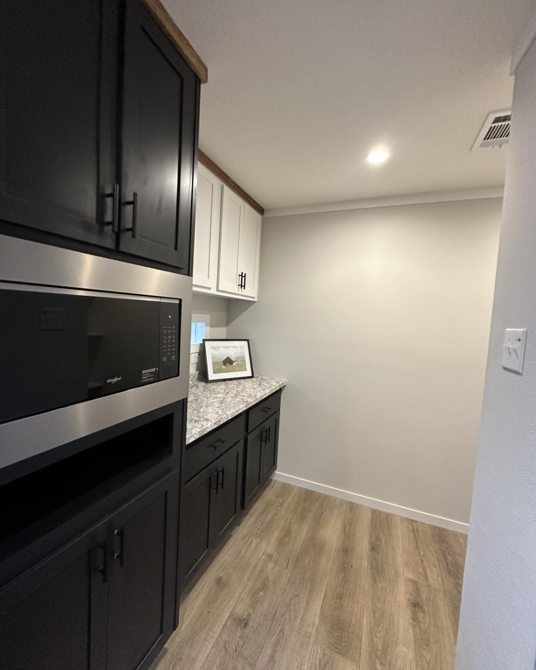 Modern kitchen with dark and white cabinets, a silver microwave, and a granite countertop. Wood floor adds warmth to the clean, minimalist design.