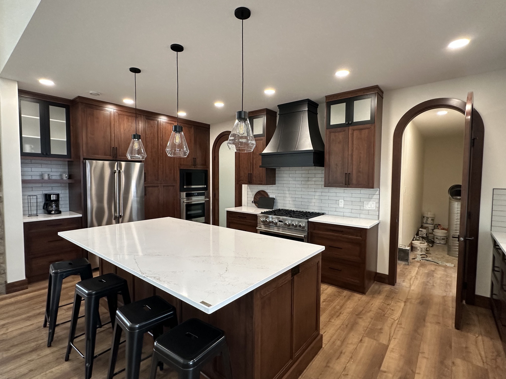 Spacious kitchen with dark wood cabinets, a large marble island, and black stools. Stainless steel appliances and pendant lights create a modern, inviting atmosphere.