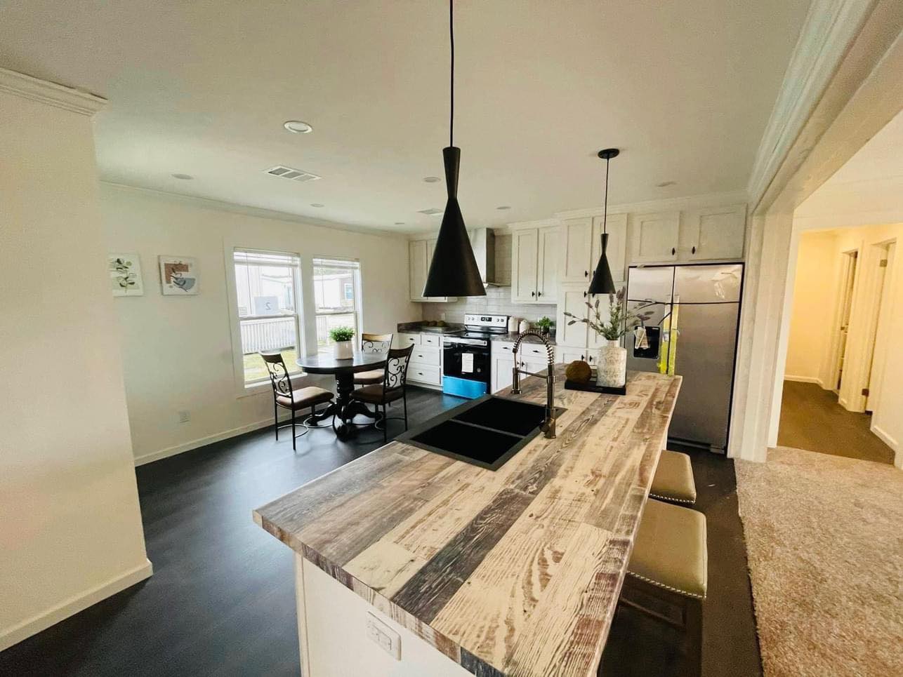 Bright kitchen with rustic wood island, black pendant lights, and stainless steel appliances. Cozy dining area near windows adds a welcoming vibe.