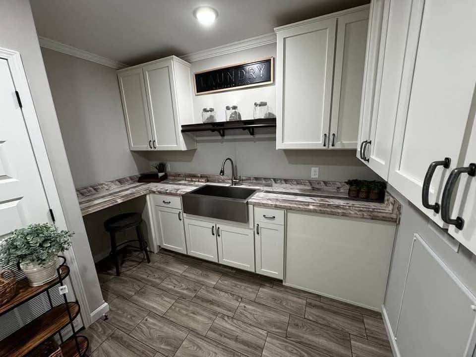 Modern laundry room with white cabinets, a stainless steel farmhouse sink, and marble countertop. A "Laundry" sign hangs above, creating a cozy feel.