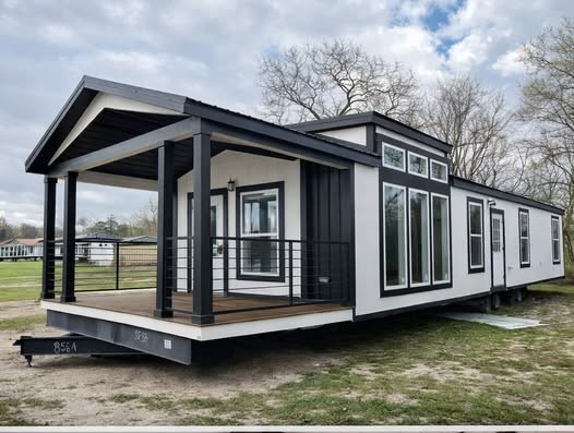 Modern tiny house with black and white exterior, large windows, and a covered porch. Set on grassy land under a cloudy sky, conveying a modern, cozy vibe.