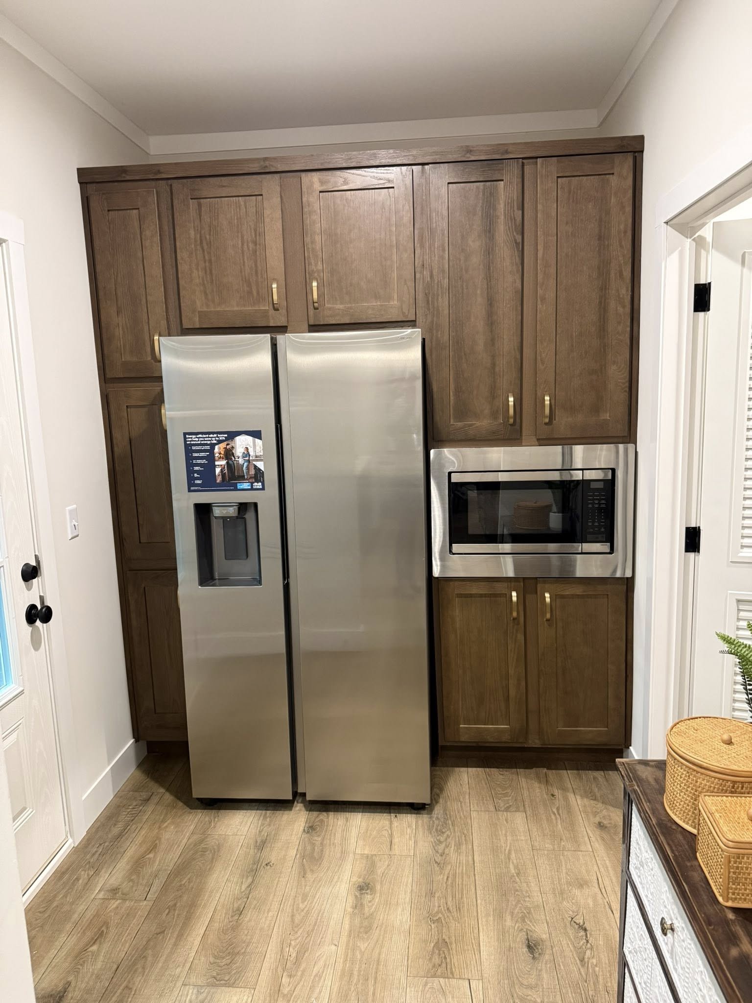A wooden kitchen island with a white countertop, brochures, a bowl of candy, and decorative bottles on top. People stand nearby on a wooden floor.