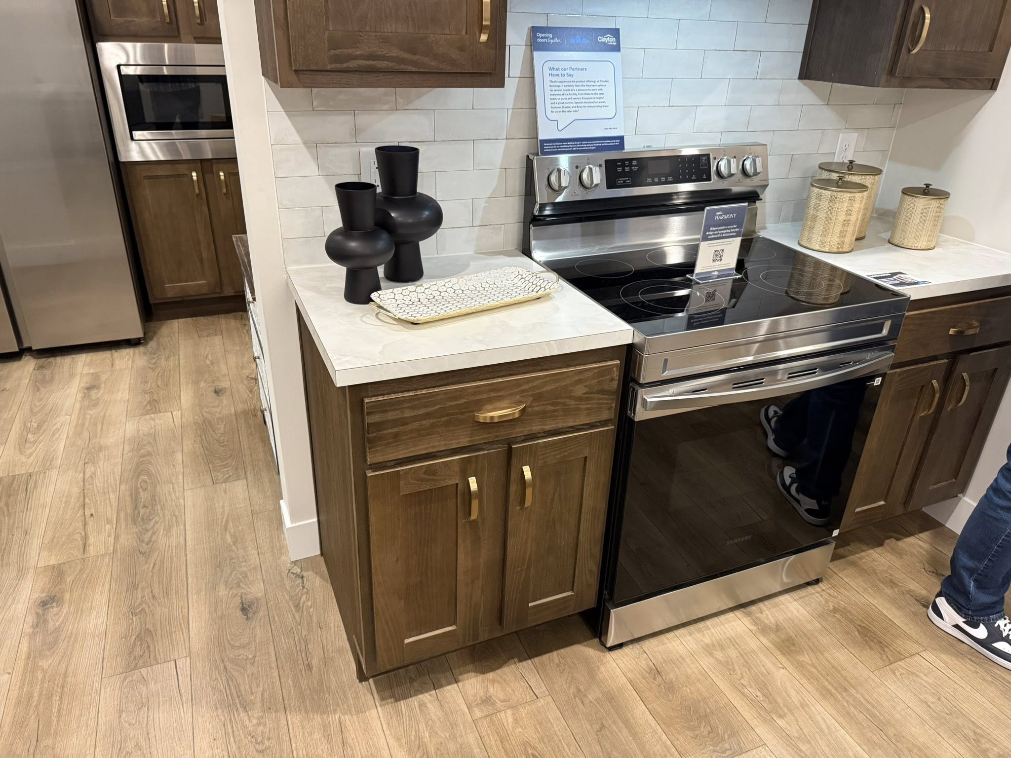 Modern kitchen with stainless steel stove, dark wood cabinets, and light countertops. Black vases and basket add decor. Hardwood floor visible.