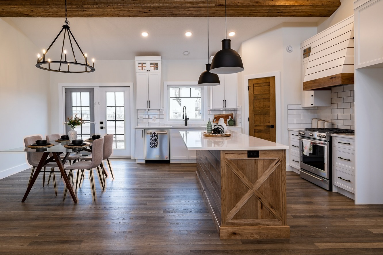 Spacious farmhouse kitchen with white cabinets, wooden island, and industrial pendant lights. Cozy dining area with modern glass table and pink chairs.