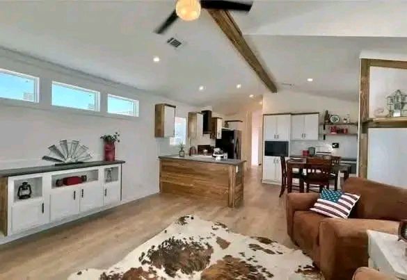 Cozy open-plan living room and kitchen with wood accents. Features a brown sofa with an American flag pillow, cowhide rug, and rustic decor, conveying a warm, welcoming atmosphere.
