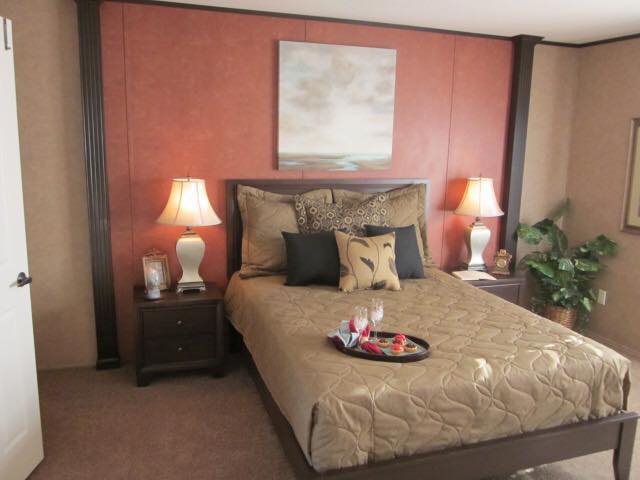 Cozy bedroom with beige bedding, decorative pillows, and a bed tray with glasses and snacks. Warm lighting from two lamps sets a serene mood.