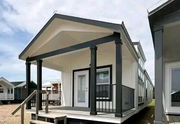 Small modern white house with a gabled roof, black trim, and pillars supporting a front porch. The sky is partly cloudy, creating a bright, inviting look.