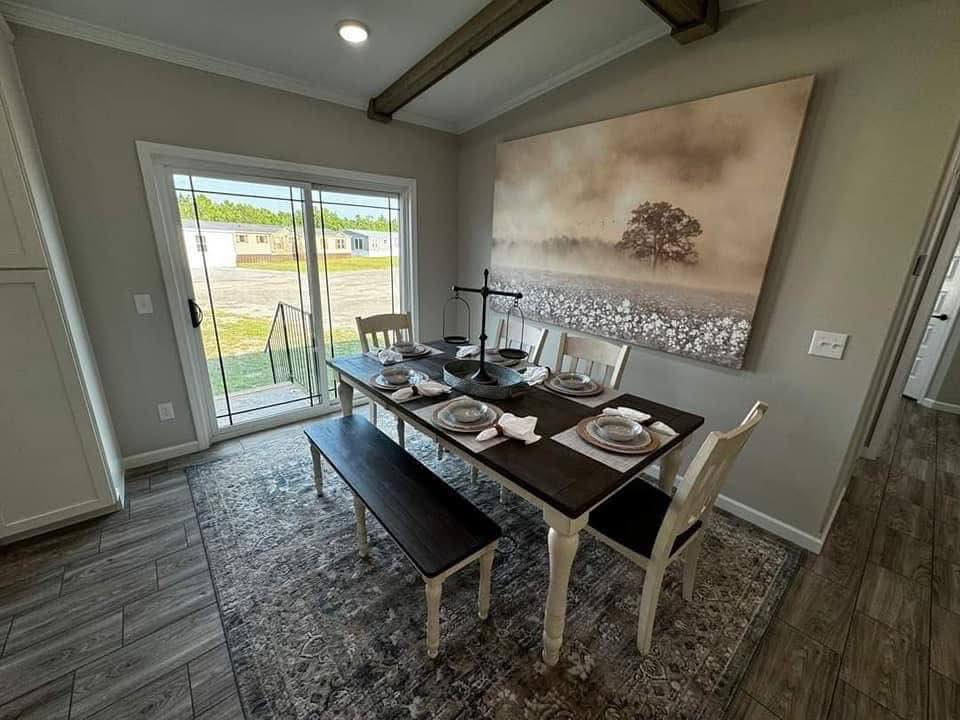 Rustic dining room with a dark wooden table set for six. A large landscape painting of a tree on a foggy field decorates the neutral-toned wall.
