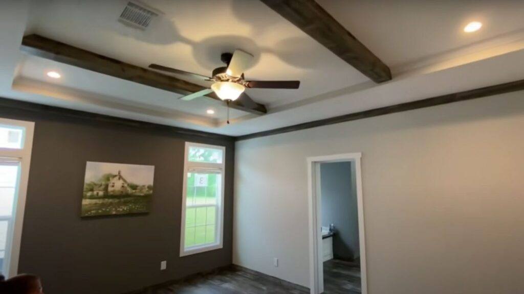 A modern room with a ceiling fan and wooden beams, soft lighting, a dark accent wall with a landscape painting, and a bright window. Calm and inviting atmosphere.