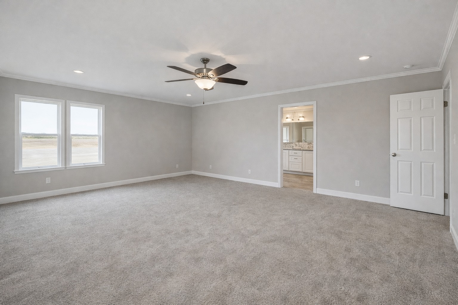 Spacious empty room with light gray walls, carpet, and a ceiling fan. Two large windows on the left and a door leading to a bright adjoining room.