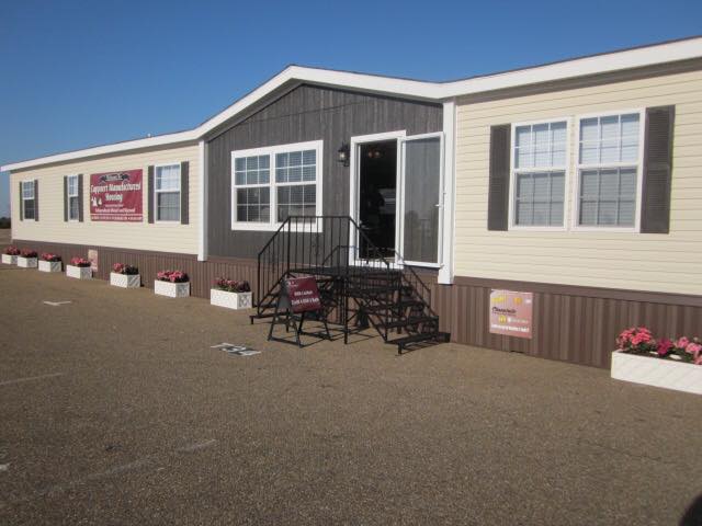 A beige and brown modular home with two doors, surrounded by flower planters. There are signs on the walls and a metal staircase leading to one door.