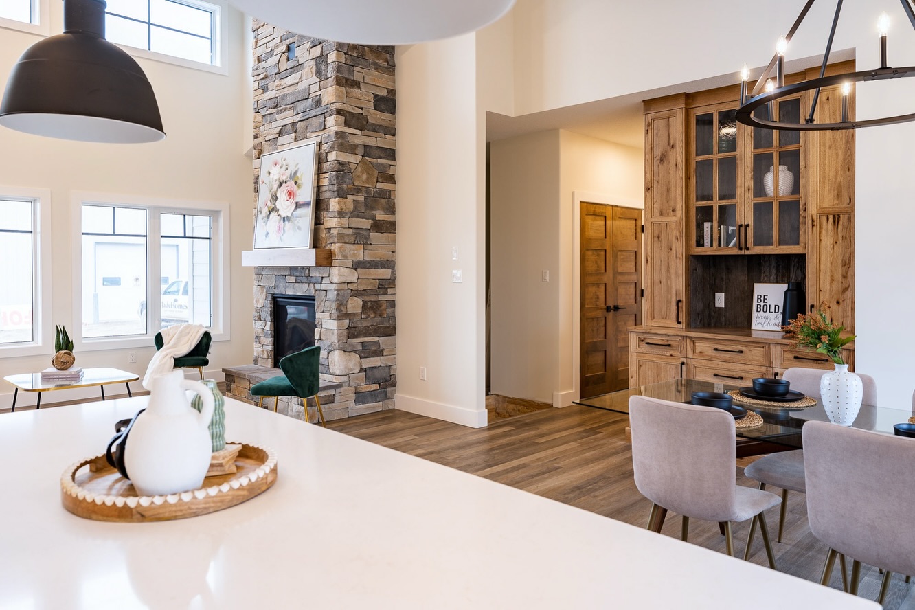 Modern living room with a stone fireplace, wooden cabinetry, and a dining table. Bright natural light, elegant decor, and a cozy, welcoming atmosphere.