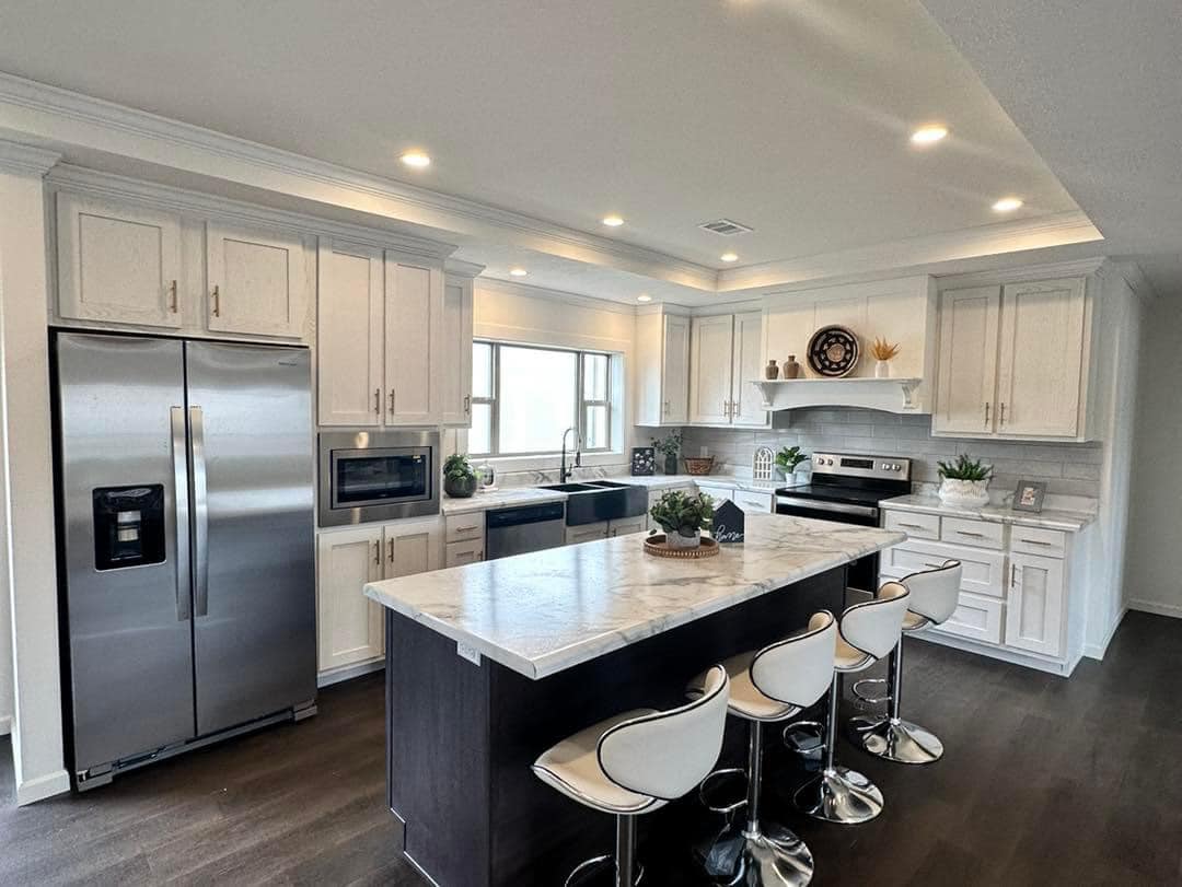 Modern kitchen with white cabinets, stainless steel appliances, and dark wood flooring. A large island with bar stools is central, creating a welcoming atmosphere.