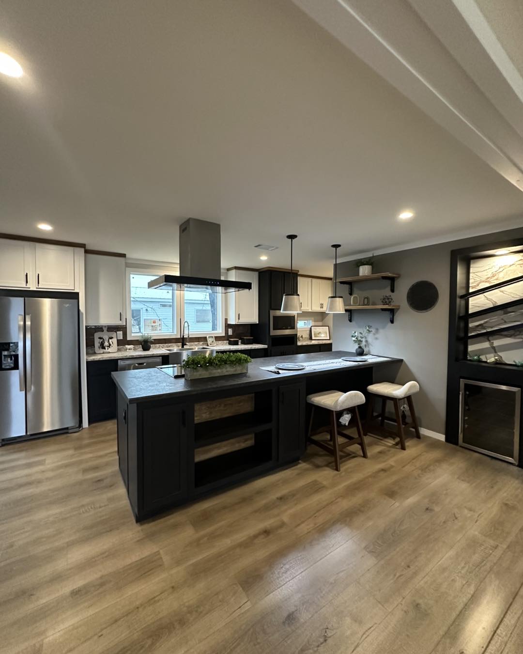 Modern kitchen with light wood flooring, black and white cabinetry, and a central island with bar stools. Pendant lights add a cozy ambiance.