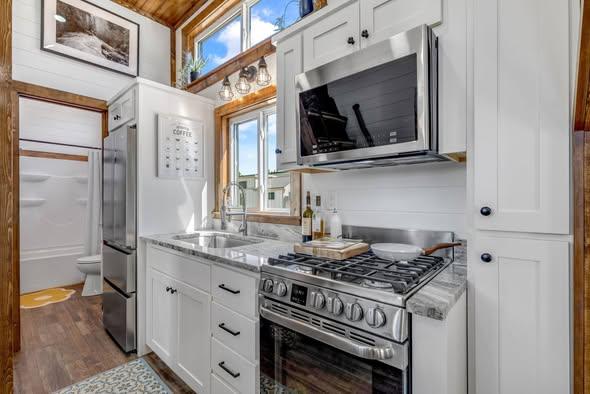 Compact, modern kitchen with white cabinets, stainless steel appliances, and wood accents. Sunlight streams in, creating a bright, inviting atmosphere.