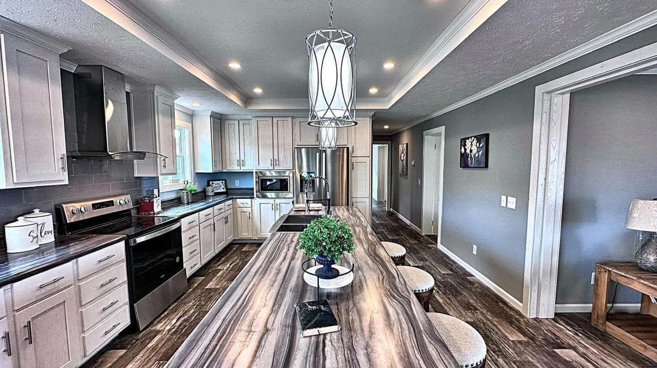 Sleek kitchen with white cabinets, stainless steel appliances, and a long marble island featuring a plant centerpiece. Modern pendant light above. Cozy, inviting atmosphere.