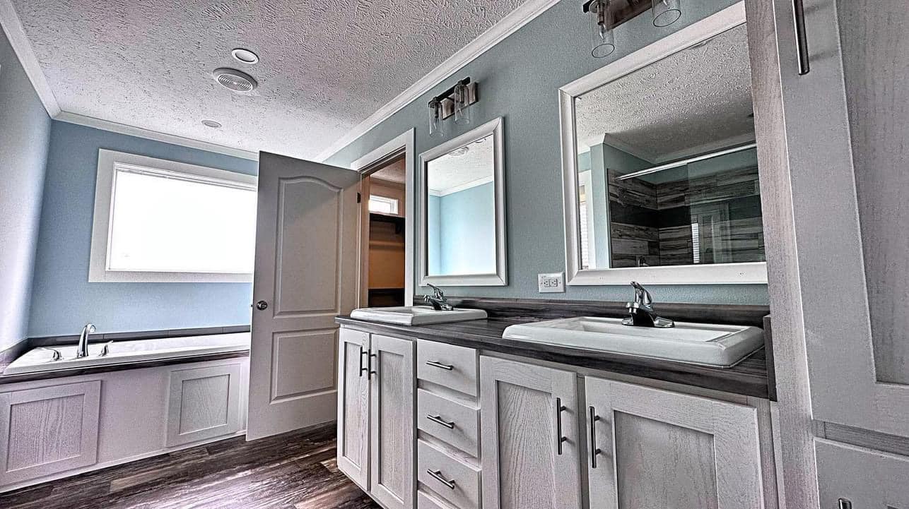 A modern bathroom with two rectangular mirrors above dual sinks on a dark countertop. A closed door, large bathtub, and soft lighting create a serene atmosphere.