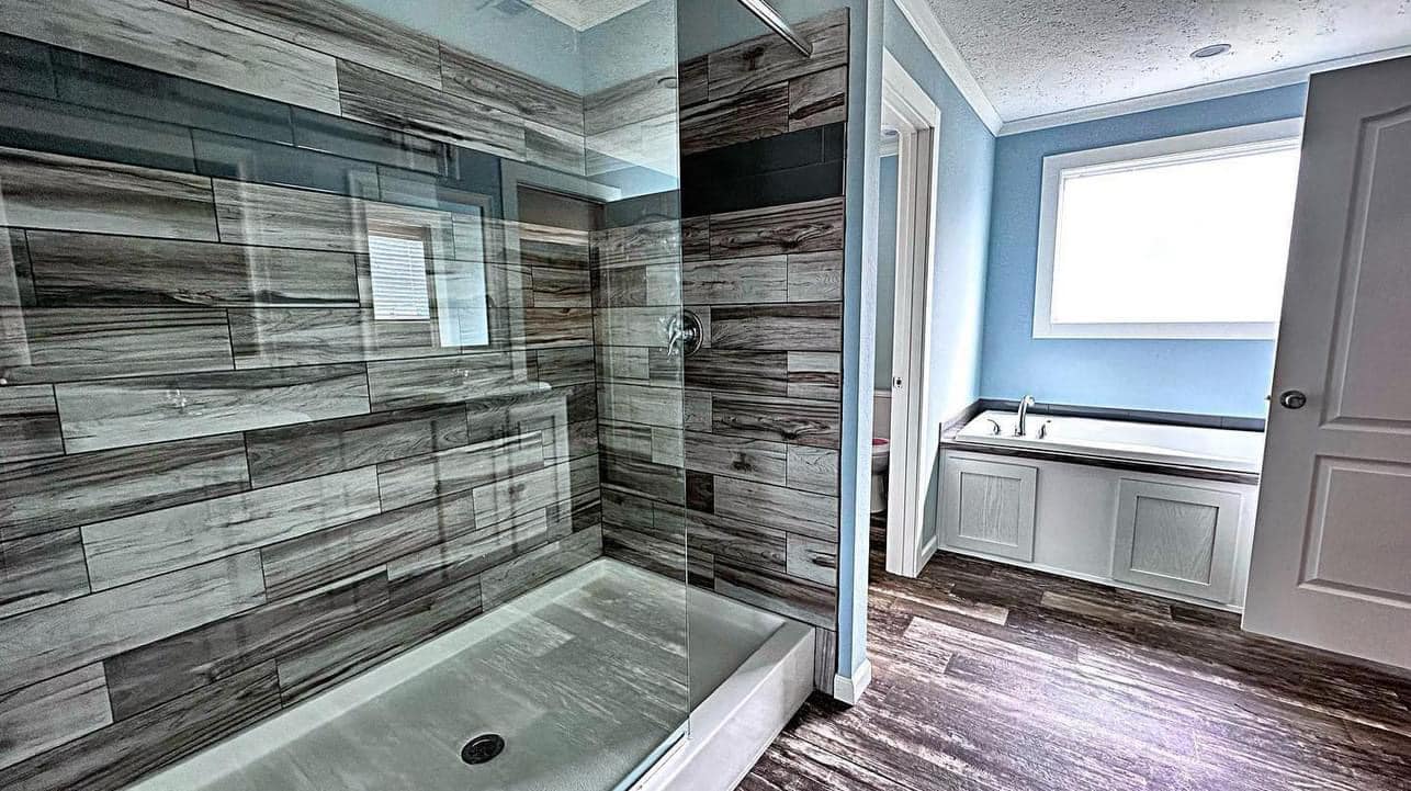 Modern bathroom featuring a glass-enclosed shower with wood-pattern tiles, a white bathtub beneath a large window, and wood-style flooring.