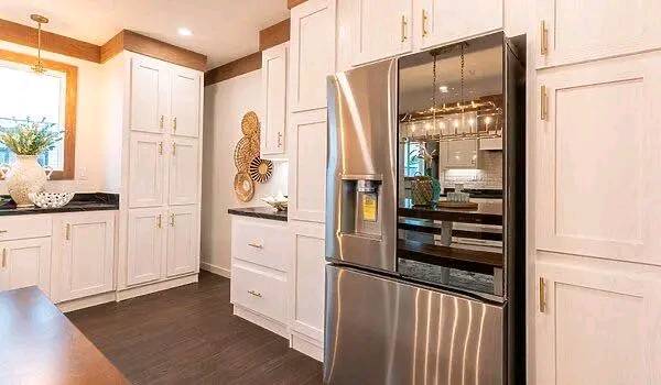 Modern kitchen with stainless steel French door refrigerator, white cabinets, and dark wood floors. Bright, airy ambiance with decorative wall accents.