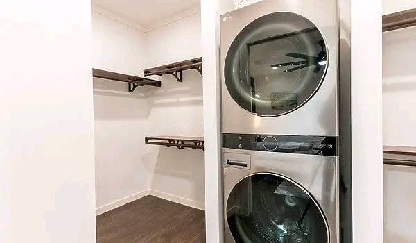 Modern laundry room featuring stacked stainless steel washer and dryer on the right. Open shelving on the left adds storage space. Clean, minimalistic design.