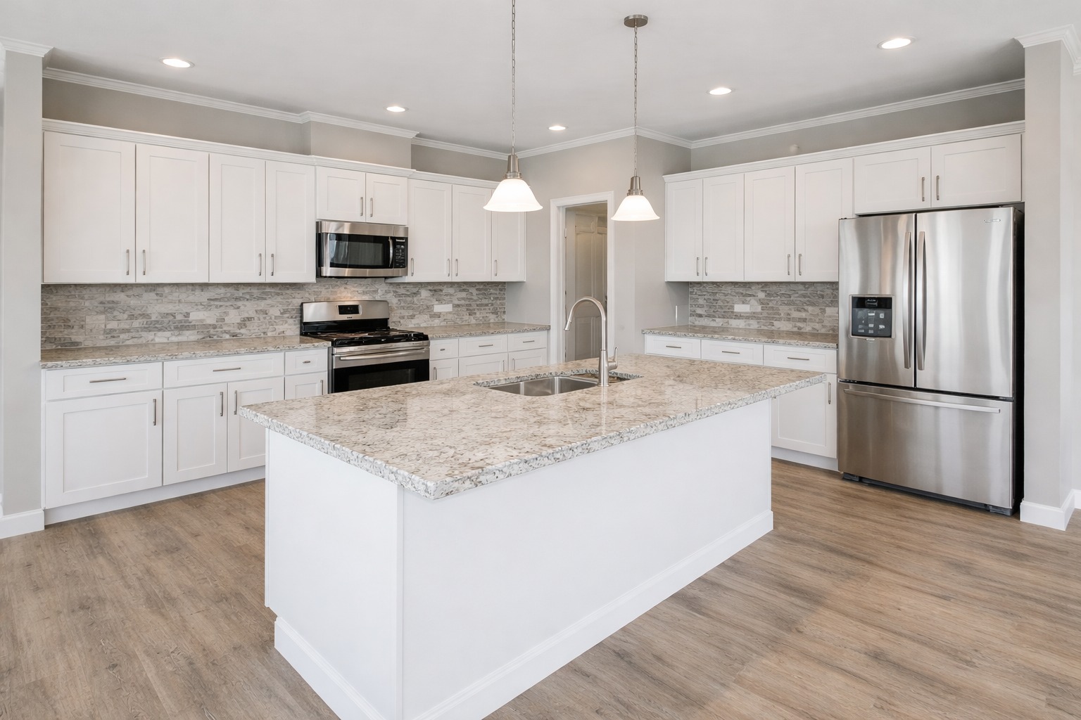 Modern kitchen with white cabinets, granite island, stainless steel appliances, and wood flooring. Bright, spacious ambiance with pendant lights.