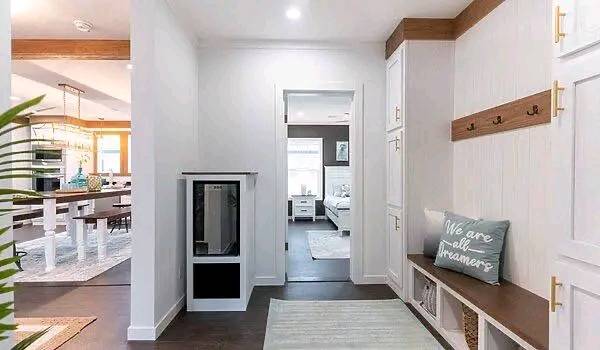 Hallway in modern home with white walls and wood accents. A cozy bench with a "We are all dreamers" cushion is on the right. Dining area and bedroom visible.