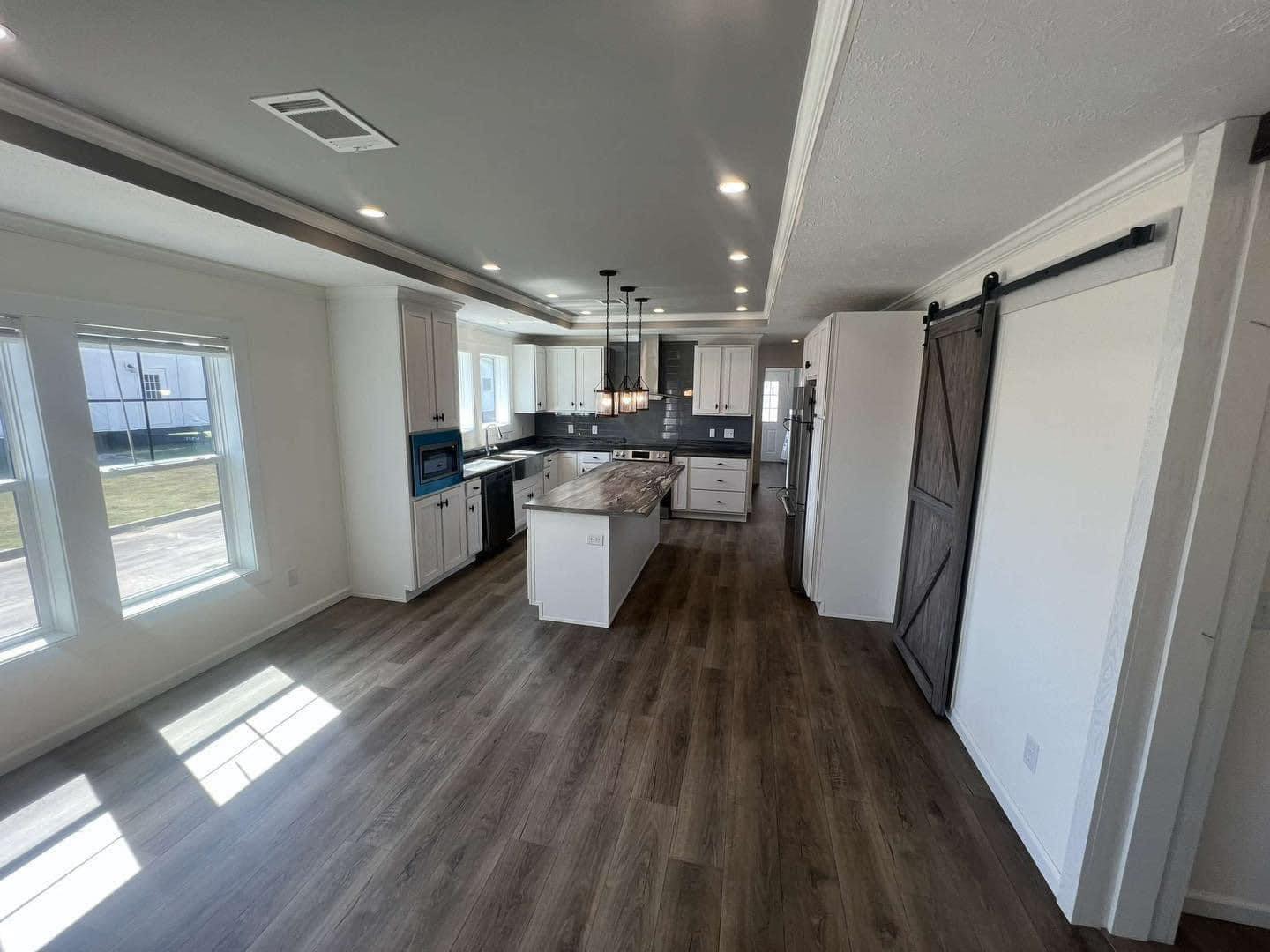 Spacious modern kitchen with white cabinets, dark countertops, and a center island. Wooden floors and large windows create a bright, inviting space.