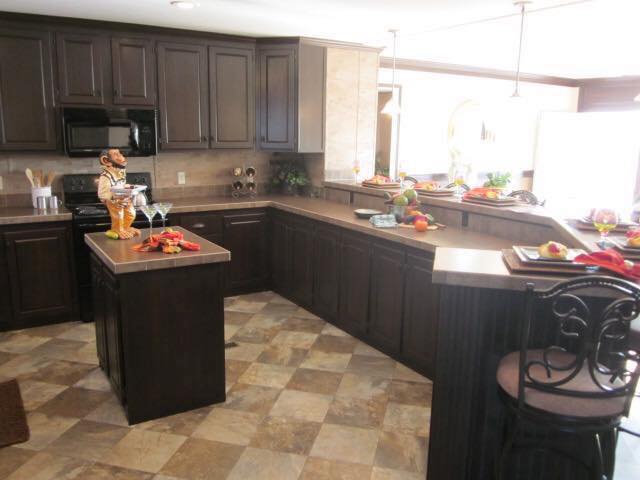 Spacious kitchen with dark wood cabinets and beige tiled floors. The countertops are adorned with colorful fruits and elegant glassware, creating a welcoming and warm atmosphere.