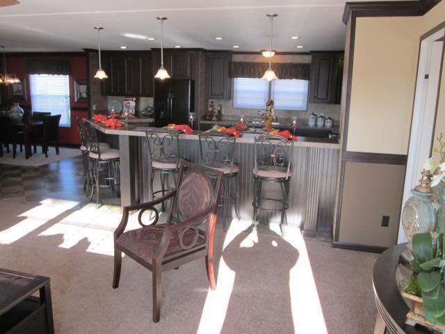 Spacious kitchen and dining area with warm lighting. Bar stools lined at a kitchen counter, a wooden chair in the foreground, and decorative accents throughout.