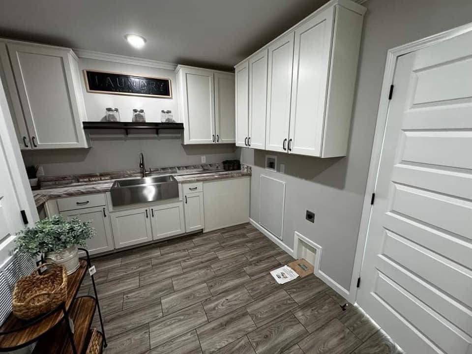 Modern laundry room with white cabinets and wooden floor. Stainless steel sink and labeled “Laundry” sign above. Clean and organized atmosphere.
