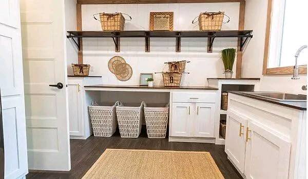 Spacious laundry room with wooden shelves holding wicker baskets, white cabinets, and four laundry hampers below. A warm, inviting ambiance with natural decor.