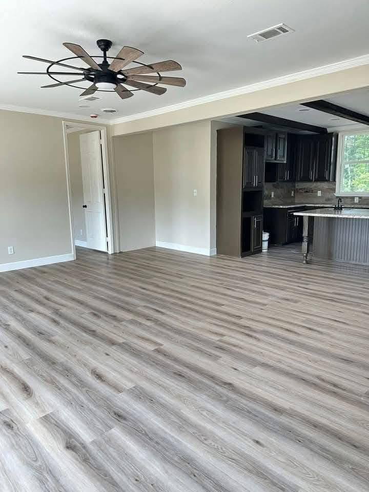 Spacious room with light wood flooring, a large ceiling fan, and an open kitchen featuring dark cabinets and a granite countertop, conveying a modern, airy feel.
