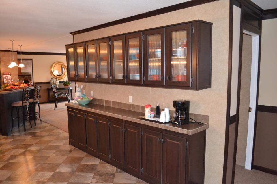 Elegant kitchen with dark wood cabinets and tiled counters, featuring a coffee maker and supplies. Warm lighting creates a cozy atmosphere.