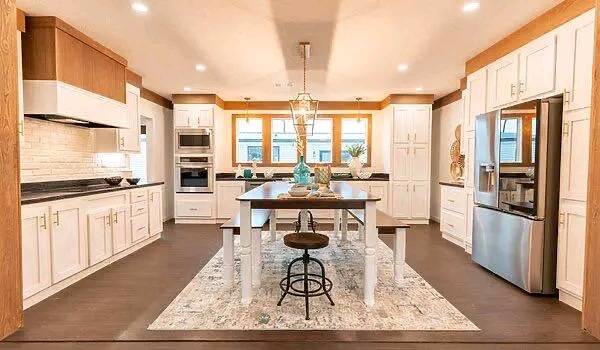Spacious modern kitchen with white cabinets, central wooden island with a decorative bowl, and stainless steel appliances. Warm lighting creates a cozy ambiance.