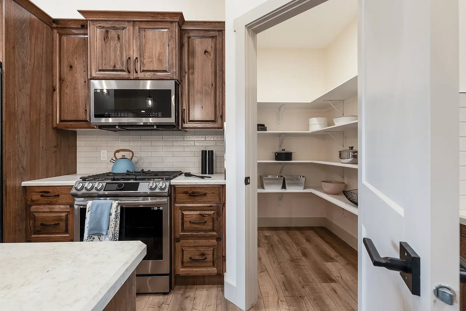 Kitchen with wooden cabinets and stainless steel stove, adjacent to an open pantry with white shelves holding kitchen items. Cozy and organized atmosphere.