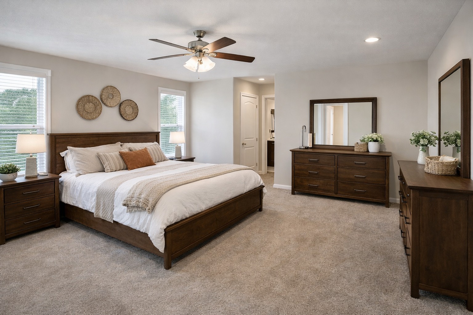 Warm, inviting bedroom with a large wooden bed, cozy white bedding, and neutral tones. Two windows, ceiling fan, dresser with mirror, and thoughtful decor.