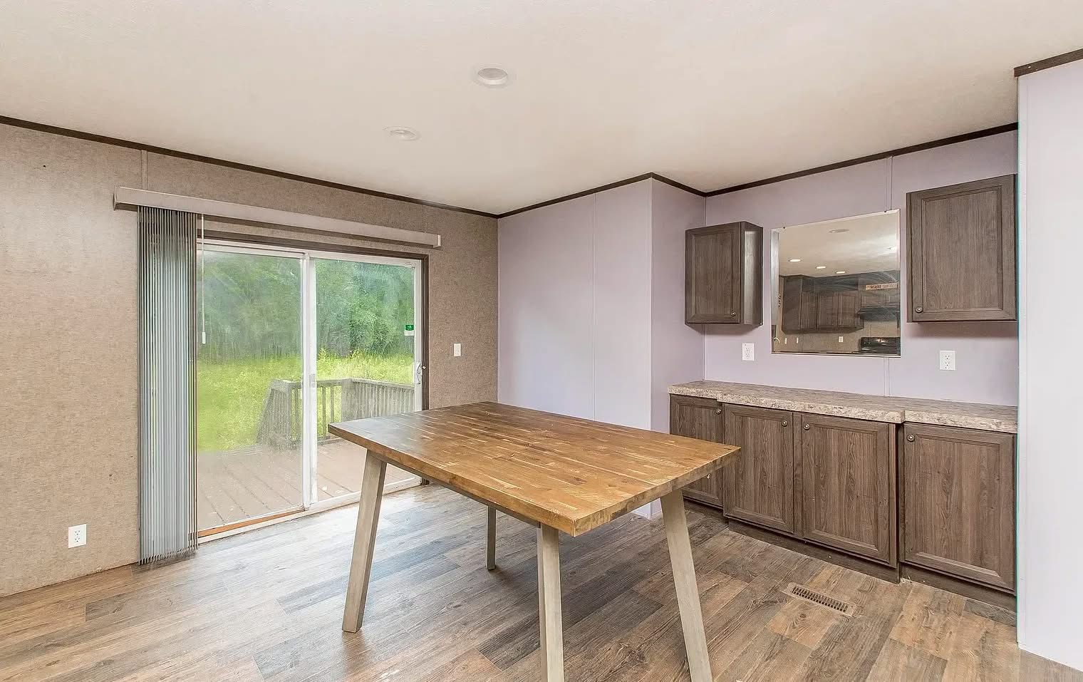 Modern dining area with a wooden table, hardwood floors, and brown cabinetry. Glass sliding doors open to a lush green outdoor view, creating a serene ambiance.