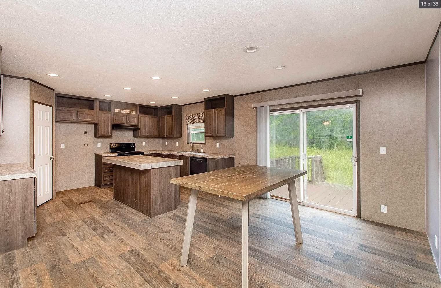 Spacious kitchen with wooden cabinets, center island, and a matching wooden table. Large sliding glass door opens to a deck, offering natural light.