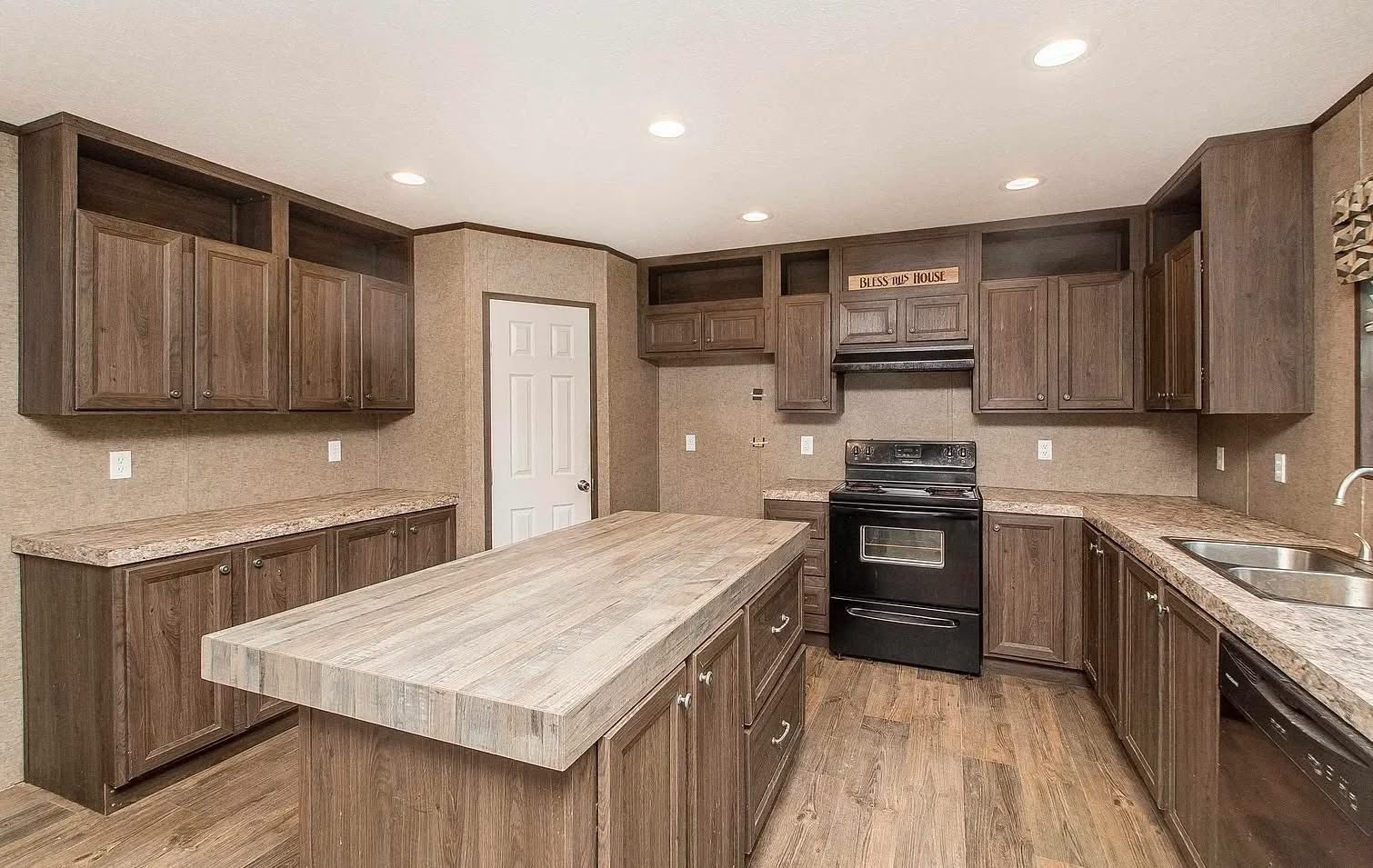 Spacious kitchen with wooden cabinets, a large central island, and a black stove. The countertops are marbled, and the room is well-lit, conveying a warm, inviting tone.